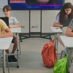 Group of students in a classroom focused on laptops at their desks, working on assignments.