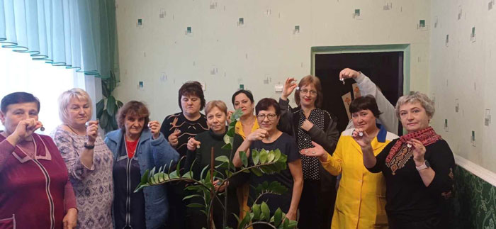 Group of about twelve adults indoors, holding up small glasses and smiling for a group photo.