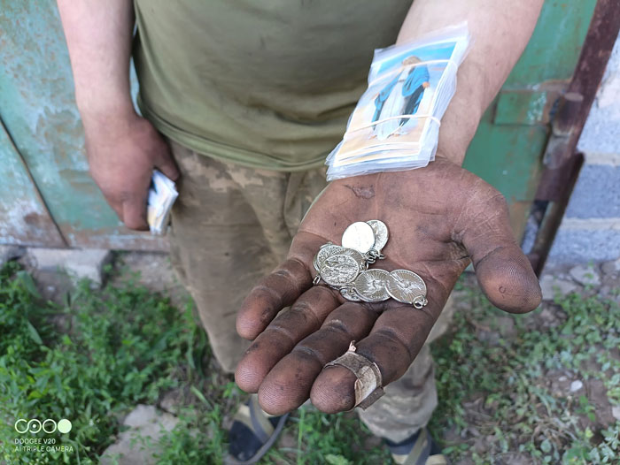 Open dirty palm holding several coins with a bandaged finger; a stack of photo cards rests on the forearm.