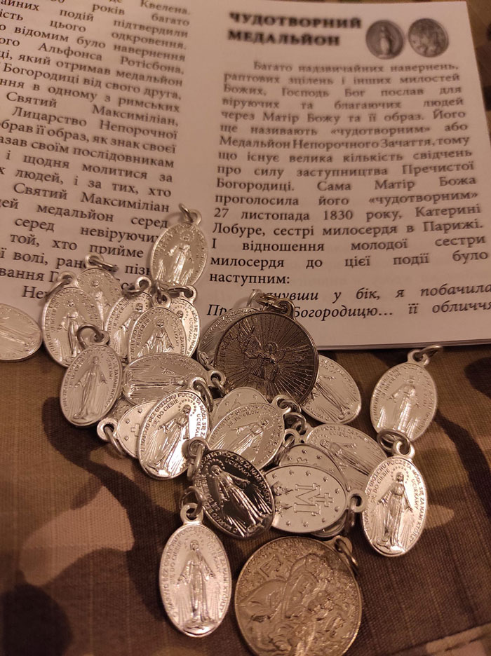 Religious medals scattered on a page of Ukrainian text, some showing figures, others with icons and inscriptions, metal reflections visible.