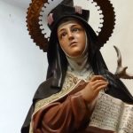 Statue of a veiled saint holding an open manuscript, gazing upward in a church interior