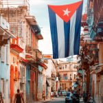 Cuban street lined with colorful colonial buildings and a large Cuban flag hanging above.