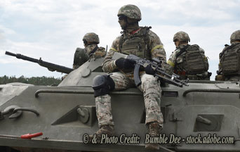 Three soldiers in camouflage sit on a military armored vehicle with a mounted machine gun under a cloudy sky.